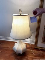 Front view of the lamp showing illuminated ivory fabric shade and ceramic base