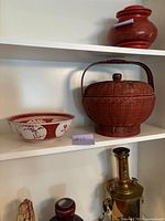 Photo showing vintage oriental wicker basket with lid and handle beside antique red and white ceramic dish on shelf.