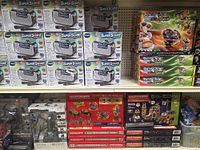Photo showing various boxed toys including VTech Super Sound Karaoke devices, Beyblade Burst toys, and Magformers construction sets on retail shelves.