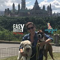 Outdoor photo with a woman holding two dogs near city landmarks, showing branding for Easy Breezy Dog Training and partner Enriched Dogs.
