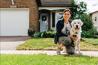 Trainer kneeling on a lawn beside a Golden Retriever wearing Easy Breezy Dog Training shirt in front of a house