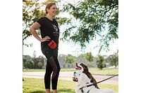 Photo of a female trainer smiling and interacting with two dogs outdoors during a training session.