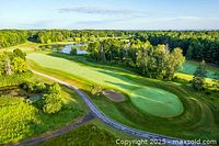 Aerial view of a golf course fairway, putting green, and water hazards with trees and stone paths, showing the natural setting and course layout.