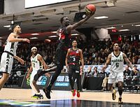 Action shot of Ottawa Blackjacks player in black and red uniform mid-air attempting a layup against Niagara players in white and green uniforms during a basketball game at TD Place.