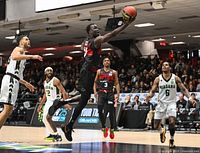 Action basketball game photo showing Ottawa BlackJacks player leaping with basketball, surrounded by Niagara team players, indoor arena setting with crowd.