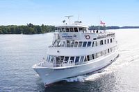 View of a white multi-deck sightseeing cruise ship underway on calm water with green shorelines and clear sky.