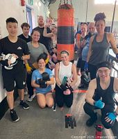 Group of trainees in boxing workout with gloves, wraps, and punching bag in gym setting.