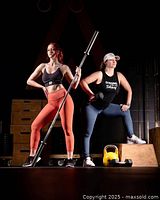 Image of two women in athletic wear posing with fitness equipment, depicting strength training and workout environment.