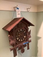 Full view of wooden cuckoo clock hanging, showing overall form and chains