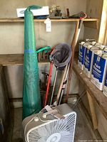 Shelf with paint thinner cans, fan, long-handle tools and green bag