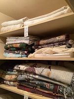 Two shelves filled with assorted folded blankets, quilts, throws showing variety of colors and fabrics
