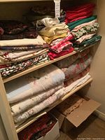 Three shelves filled with folded quilts, sheets and fabrics plus box of fabric remnants