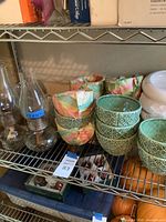 Shelving with two stacks of green ceramic bowls, three clear glass oil lamps, tray of red ornaments visible