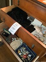 Drawer view showing blue tray filled with multiple brooches, pins, green jewelry case, crocheted lace