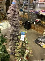 Tall tinsel tree and smaller pine tree shown together in storage area