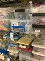 Multiple clear storage bins on metal shelving filled with assorted craft materials