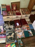 Overview of three bankers boxes filled with assorted vintage hardcovers and several books and puzzles laid out