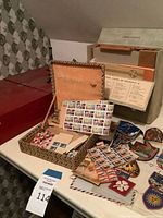 Tabletop view showing Chemcraft red case, open suitcase of stamps, Linguaphone beige case and travel patches