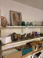 Full shelves showing framed print, glass insulators, metal animals, fish sculpture, glassware