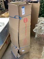 Tall cardboard box containing artificial tree, taped and tied