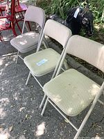 All three beige folding chairs lined up side by side outdoors