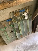 Two stained glass panels leaning against wall showing floral motifs and size labels