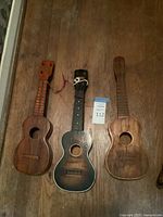 Three wooden ukuleles laid side by side showing overall condition