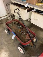 Overall view of red pull wagon containing various metal parts