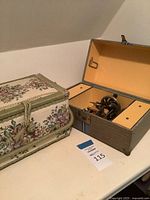 Singer miniature sewing machine inside gray carry case next to floral tapestry sewing box