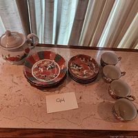 Full view of the set showing 4 teacups, 4 saucers, 3 plates and a teapot arranged on a table.