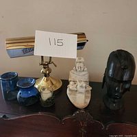 Photo showing all items on a wooden surface: wooden African sculpture, ceramic sculpture, brass lamp, two blue ceramic candle holders, and one glass candle holder.