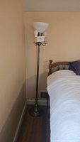 Full view of the brass floor lamp next to a bed, showing its height and design of the base and pole.