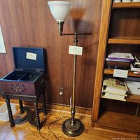 Full view of the brass swing arm floor lamp next to a wooden box and bookshelf showing overall size and condition.