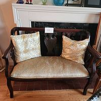 Full front image of vintage tea couch with two gold fabric pillows, showing carved wood frame.