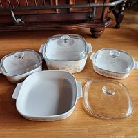 Full view of 4 ceramic Corningware dishes with floral pattern and 4 clear glass lids, 3 lids on dishes and 1 lid set aside.