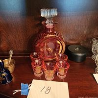Photo showing ruby crystal decanter with etched flower design and ribbed sides, accompanied by five matching ruby glass shot glasses.