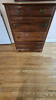Front view of wooden dresser with seven drawers and antique metal handles.