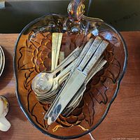 Top view of utensils including 5 forks, 5 spoons, and 5 cutting knives in amber glass fruit bowl with floral decoration.