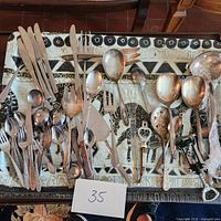 Overview of assorted flatware spread on fabric with various knives, forks, spoons, serving utensils and specialized kitchen tools.
