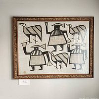 Full view of framed African mud cloth art showing abstract bird and human figures with dark cork frame border.