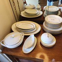 Full set of stacked plates, platters, covered casserole dish, and gravy boat displayed on wooden surface