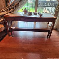 Front view of the wooden buffet table with marble inlay top and decorative teacup set on top, showing overall shape and lower shelf
