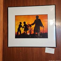 Framed art print showing silhouettes of Mary Bethune and two children at sunset hung against wooden wall with a white mat and black frame.