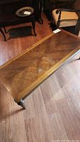Rectangular wooden coffee table with a glass top on wooden plank floor. Table has a visible wood grain and tapered legs ending in metal caps.