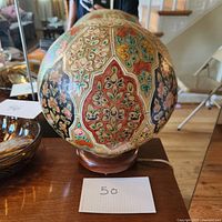 Front view of the round camel skin lamp showing detailed hand painted floral patterns in red, yellow, green, black, and blue on cream background.