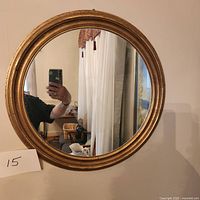 Full view of the round mirror with rustic gold painted wood frame hanging on a wall.