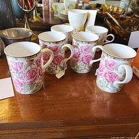 Four Royal Bone China mugs displayed on a wooden surface with visible pink rose designs and gold accents.