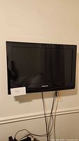 Front view of 30-inch Samsung black flat-screen TV mounted on wall with cables hanging below.