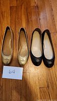 Two pairs of flat shoes on wooden floor: one gold pair and one black pair, both size 6.5 and by Coach brand.