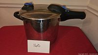 Photo showing front side of stainless steel pressure cooker with black handles and blue pressure valve.